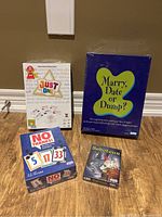 Four new board games in packaging on floor: Just One, Marry Date or Dump?, No Thanks, Saboteur
