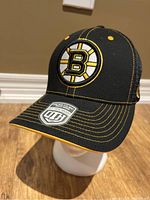 Front angle showing Boston Bruins logo embroidered on front black panel with yellow stitching on the brim and cap body above the brim.