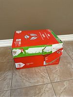 Box containing 10 packs of Staples legal size copy paper with visible box wear.