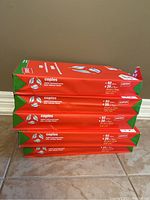 Five unopened packs of Staples copy paper stacked horizontally on a tile floor against a wall.