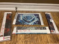 Four rolled diamond art canvases showing printed designs including a blue rose and floral patterns, laid flat on wooden floor.