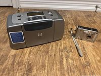 HP photo printer and HP Photosmart R707 digital camera side by side on floor