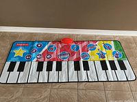 Full view of large colorful Fisher-Price piano mat with black and white keys and interactive music buttons around the top edge.