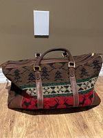 Front and side view of the woven MAGGIB tote bag showing pattern, leather handles, and gold-tone hardware.