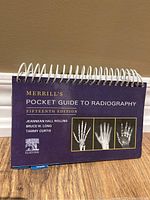 Front cover of Merrill's Pocket Guide to Radiography, Fifteenth Edition, purple cover with spiral binding and hand X-ray images.