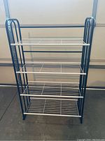 Front view of metal storage shelf showing four white wire shelves and blue frame.