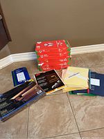 Photo showing five reams of 8.5x14 paper stacked, some with torn wrappers, alongside various file folders and office supplies.