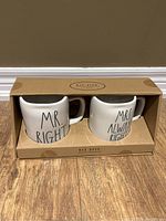 Pair of Rae Dunn ceramic mugs in original cardboard box labeled beneath with brand and collection.