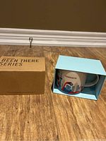Starbucks mug in light blue box with cardboard sleeve on floor showing 'Been There Series' text