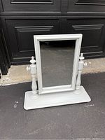 Front view of white wooden table top mirror showing rectangular glass and turned side supports on flat base.