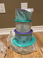 Four nested Tupperware containers with Christmas designs, lids in teal and purple, plastic wrapping partially visible