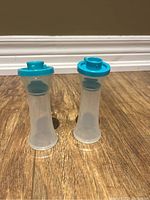 Two Tupperware salt and pepper shakers with turquoise lids on wooden floor.