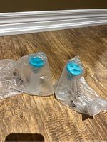 Two Tupperware salt and pepper shakers in plastic packaging on wooden floor.