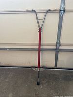 Full view showing the red metal shaft, metal handlebar with white grips, and lower part of the pogo stick.