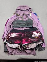 Top view of the pile showing purple jacket, grey sports bra, and multicolored pink shorts