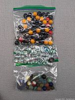 Photo showing three plastic bags with different styles of marbles: random colored marbles, clear glass marker marbles, and sea glass marbles.