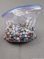 Clear zip-top bag filled with a large quantity of multicolored glass marbles.