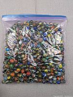 Clear zipper storage bag filled with a large quantity of colorful glass cats eye marbles.