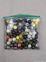 Full clear ziplock bag filled with assorted speckled glass marbles of various colors and designs.