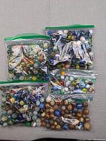 Five resealable plastic bags filled with mixed marbles of glass and clay in various colors and patterns.