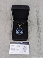 Blue topaz pendant in a black presentation box alongside certificate card from Earthmind Gemological Laboratories showing certifications and details of the gemstone.