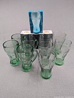 Front view of all Coca-Cola glasses showing various sizes and types including boxed glass on top.