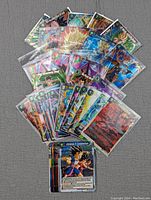 Photo of a spread collection of Dragon Ball Z trading card game cards, showing rare and foil variants with multiple character illustrations, sleeved for protection.