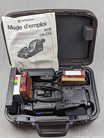 Open carrying case containing Hitachi VHSC VM-C1A camcorder, original French manual, and multiple new blank VHS-C tapes.