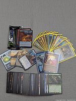 Photo showing a spread of Magic the Gathering cards including rares with yellow and black borders, some in protective sleeves, and a sealed booster pack.