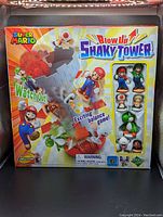 Front of box showing the Super Mario Blow Up Shaky Tower game with Mario, Luigi, Yoshi, and Toad figures visible inside the sealed packaging.