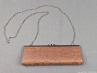 Top view of vintage orange clutch purse displaying fabric texture, metallic floral patterns, silver-tone frame and chain strap.