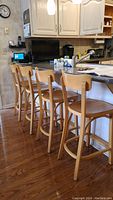 Four wooden bar stools lined up at kitchen counter, showing side view and arrangement.