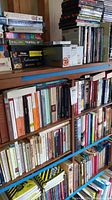 Two wooden shelves filled with fiction books in various sizes and colors, some stacked horizontally on upper shelf
