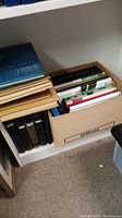 Shelf holding multiple books consisting of vintage yearbooks and genealogy-related books in used condition stored in a box and stacked.