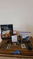 Wide view of the GoPro Hero 3+ camera, guidebook, suction mount, charging cables, memory cards, and mounts bag on wooden surface.