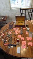 Full view of the jewelry items laid out on a wooden table including necklaces, earrings, pins and jewelry box.