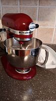 Front view of red KitchenAid Artisan mixer mounted with stainless bowl and whisk