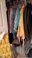 Closet with assorted hanging jackets, shirts and dresses including black leather jackets, denim jackets, and yellow raincoat.