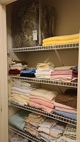 Linen collection on metal shelving with assorted folded towels, sheets, blankets, and pillowcases in multiple colors and textures.
