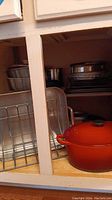 Shelf view with orange Le Creuset roaster in front, wire rack, bundt pans, and other pans in the back