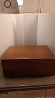 Closed wooden storage chest on countertop with lock visible, plain top surface with slight wear.