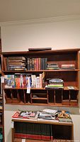 Full frontal view of wood wall hanging shelf with books and magazines inside compartments and on lower surface.