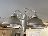 Close-up view of chandelier showing white metal construction, ribbed lamp shades, and two light bulbs visible under shades, hanging chain attached.