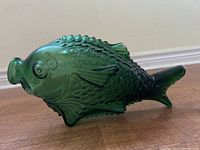 Side view of a green glass fish-shaped decanter showing detailed scales, fins, and the decanter opening at the fish's mouth.