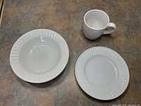 Two white ceramic bowls and one plate, all with a ribbed edge pattern, along with one white mug on a table.
