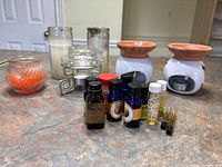 Two ceramic oil warmers, glass oil warmer, assorted candles, and various fragrance oil bottles on a countertop