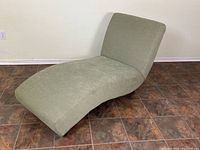 Full side view of leaf green fabric chaise lounge, showing curved ergonomic shape and angled backrest, positioned on tiled floor.