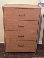 Front view of light wood finish 4-drawer dresser with black pull handles on each drawer.
