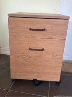 Front view of wood finish filing cabinet showing two drawers with metal handles and wheels at the base.