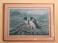 Full view of framed print depicting two dogs in a natural mountainous landscape under a blue-gray sky.
